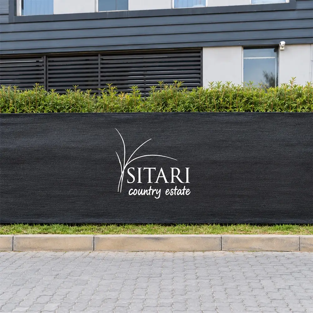 Branded black shade net fencing with white Sitari Country Estate logo installed in front of a commercial building.